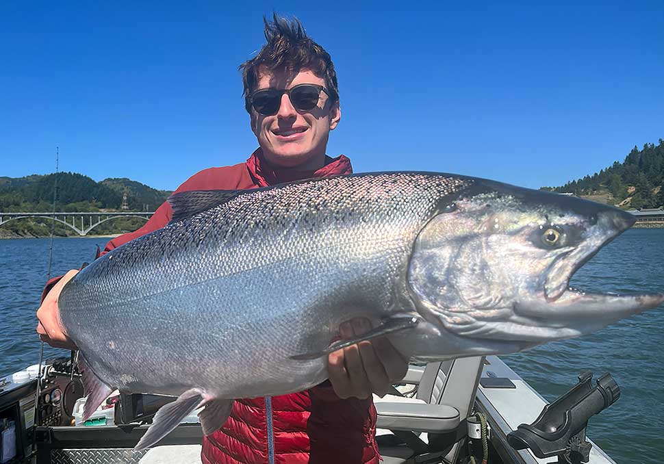 Photo of a young man holding a beautiful, shiny 25 pound King Salmon caught on the Rogue River on Tuesday, July 11, 2023